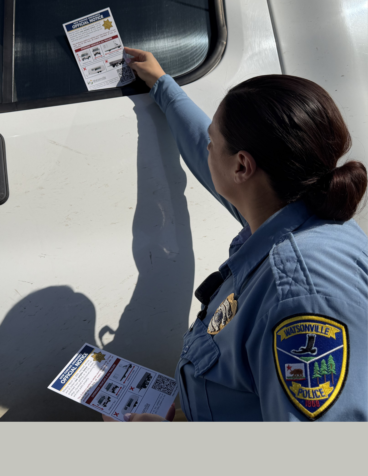 Watsonville Police Service Specialist in uniforma placing an official notice on the windshield of a 
